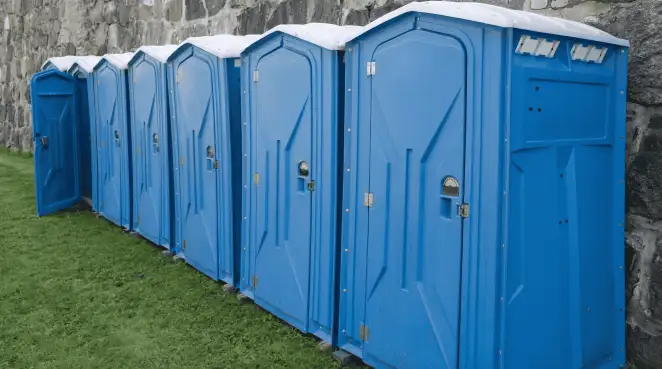 Row of blue portable toilets lined up on grass against a stone wall for event sanitation in Memphis, TN