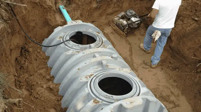 Septic tank installation showing a technician compacting soil around a new poly septic tank in an excavation pit in Memphis, TN
